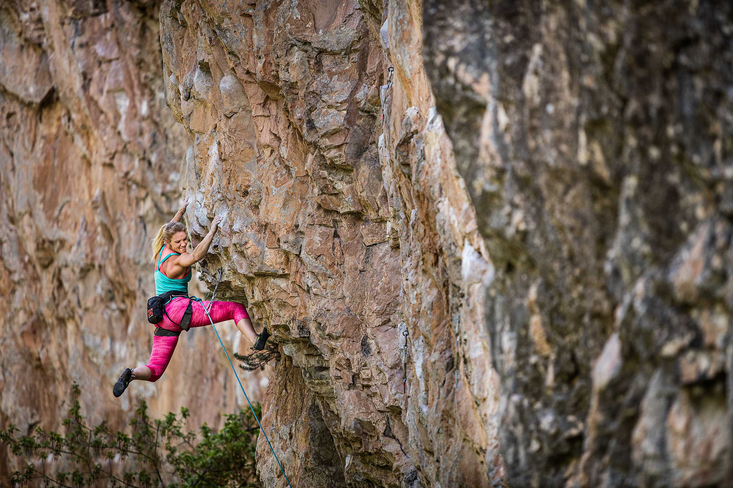 A professional female rock climber swings wildly and struggles to keep from falling 