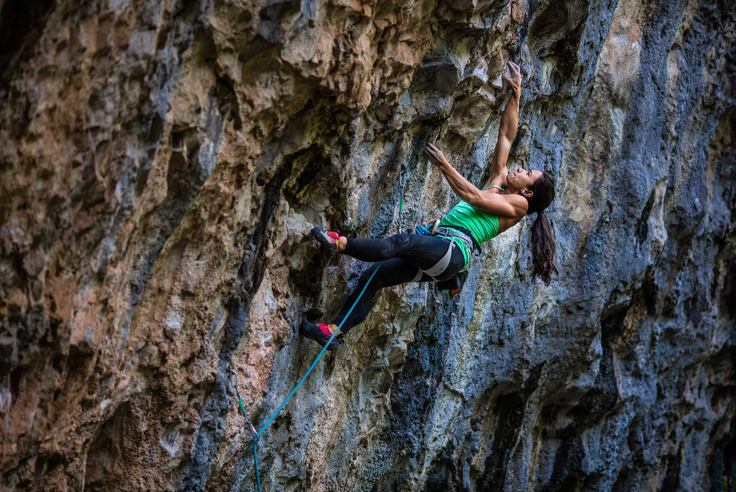 A muscular female professional rock climber makes a desperate lunge in Colorado