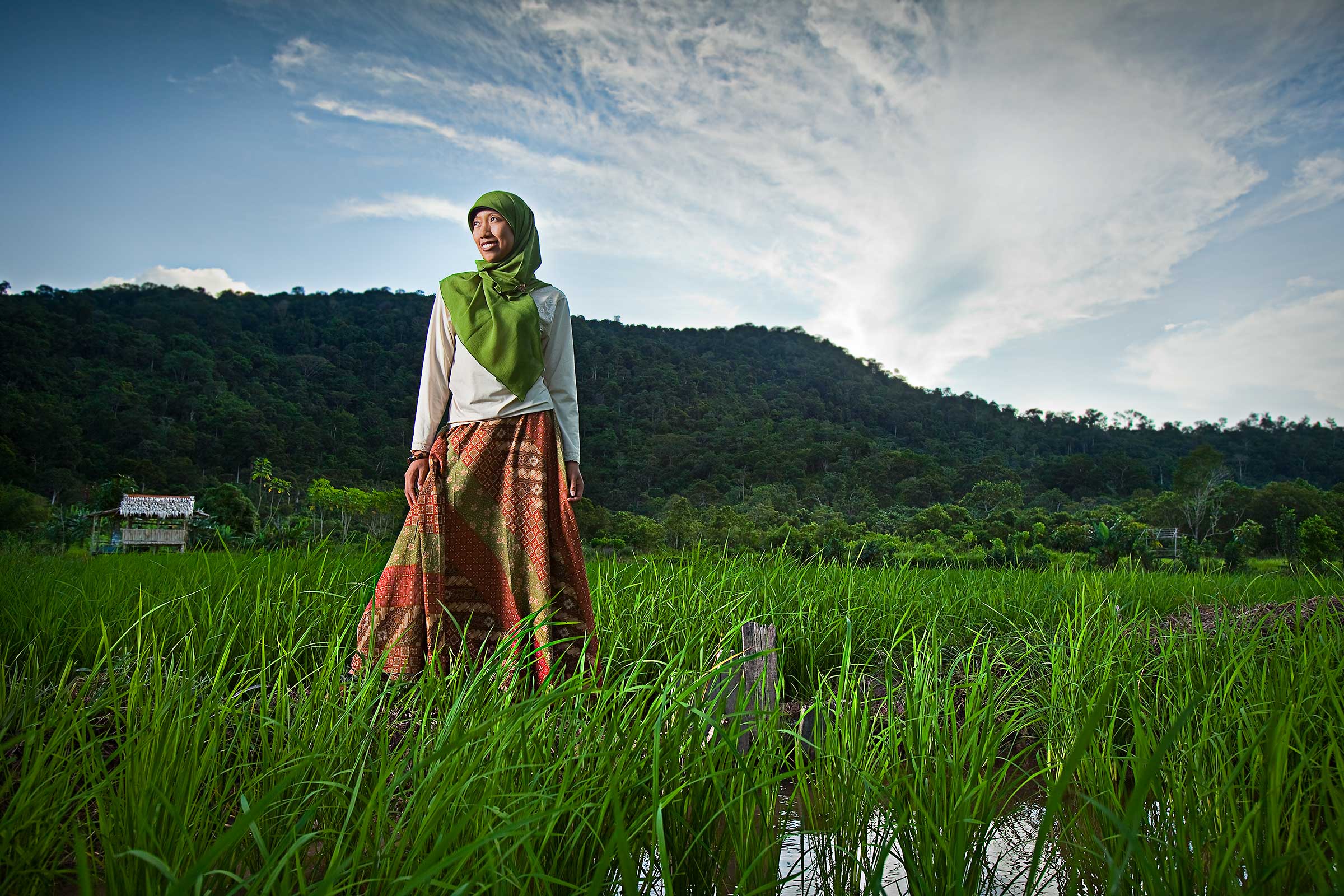a woman in beautiful traditional muslim clothing poses among rice paddies in Kalimantan Indonesia