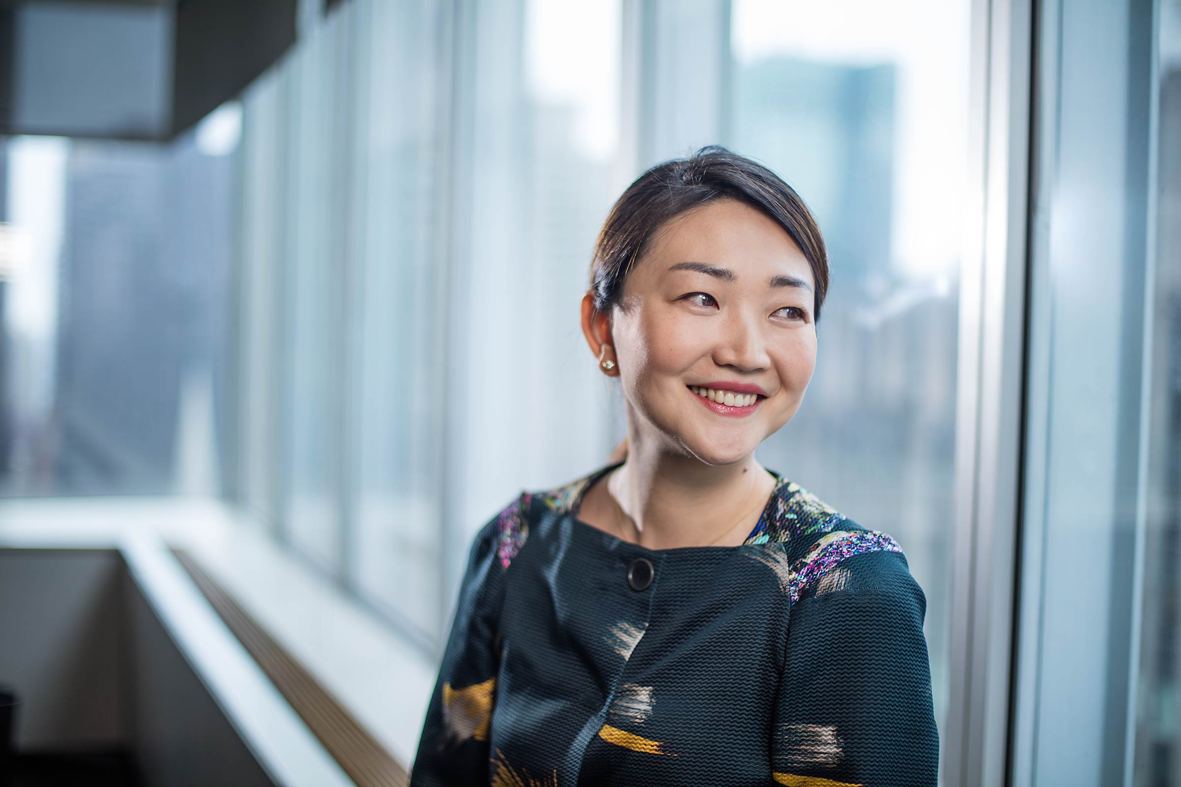 A female Asian executive smiles out the window of aNew York City office
