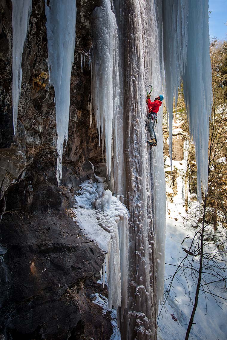 an ice climber ascends a dramatic icicle hanging from a Catskills cliff in New York