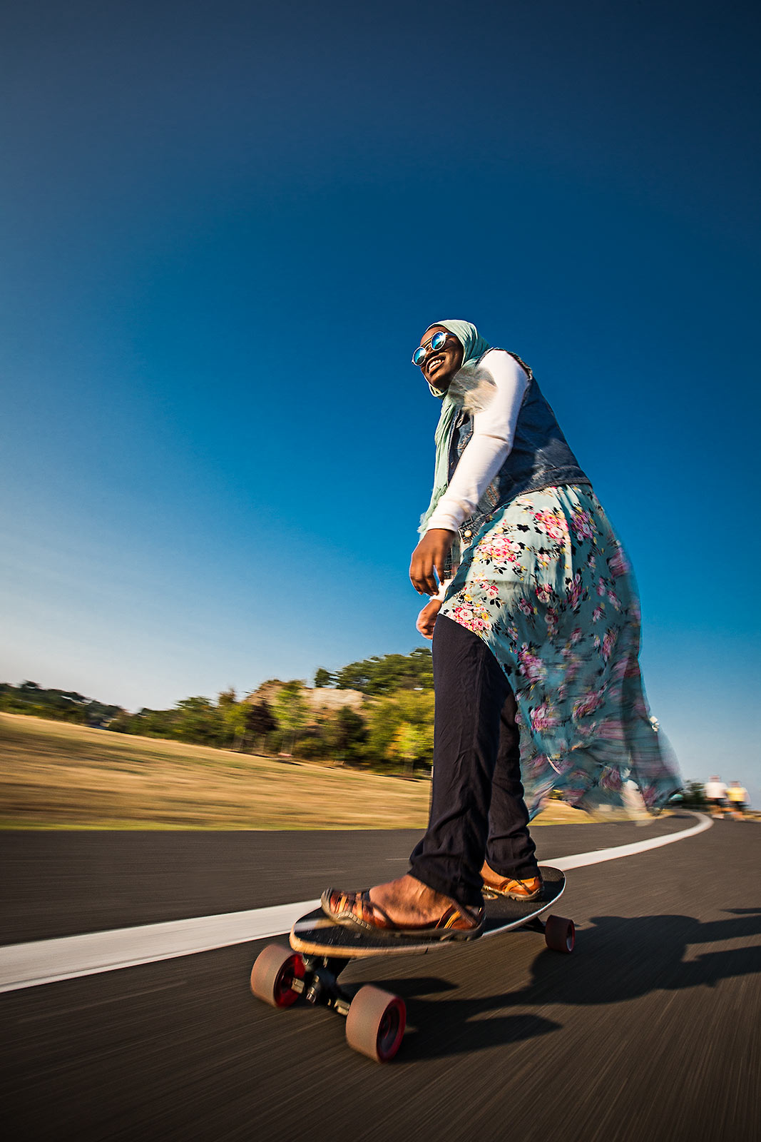A young muslim woman wearigna headscarf riding a skatebaord at a Connecticut beach