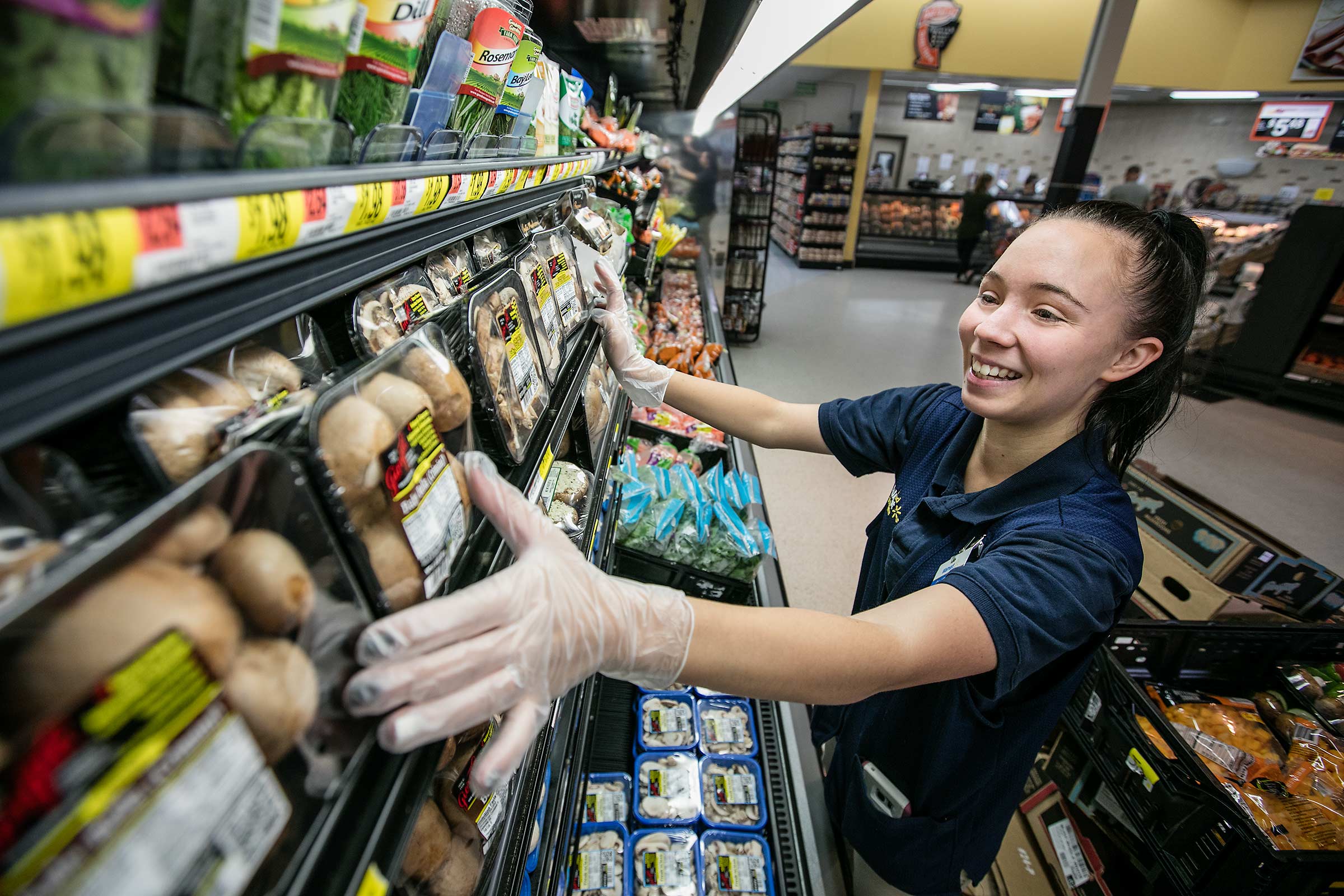A young female retail store employee smiles while stocking shelves at work