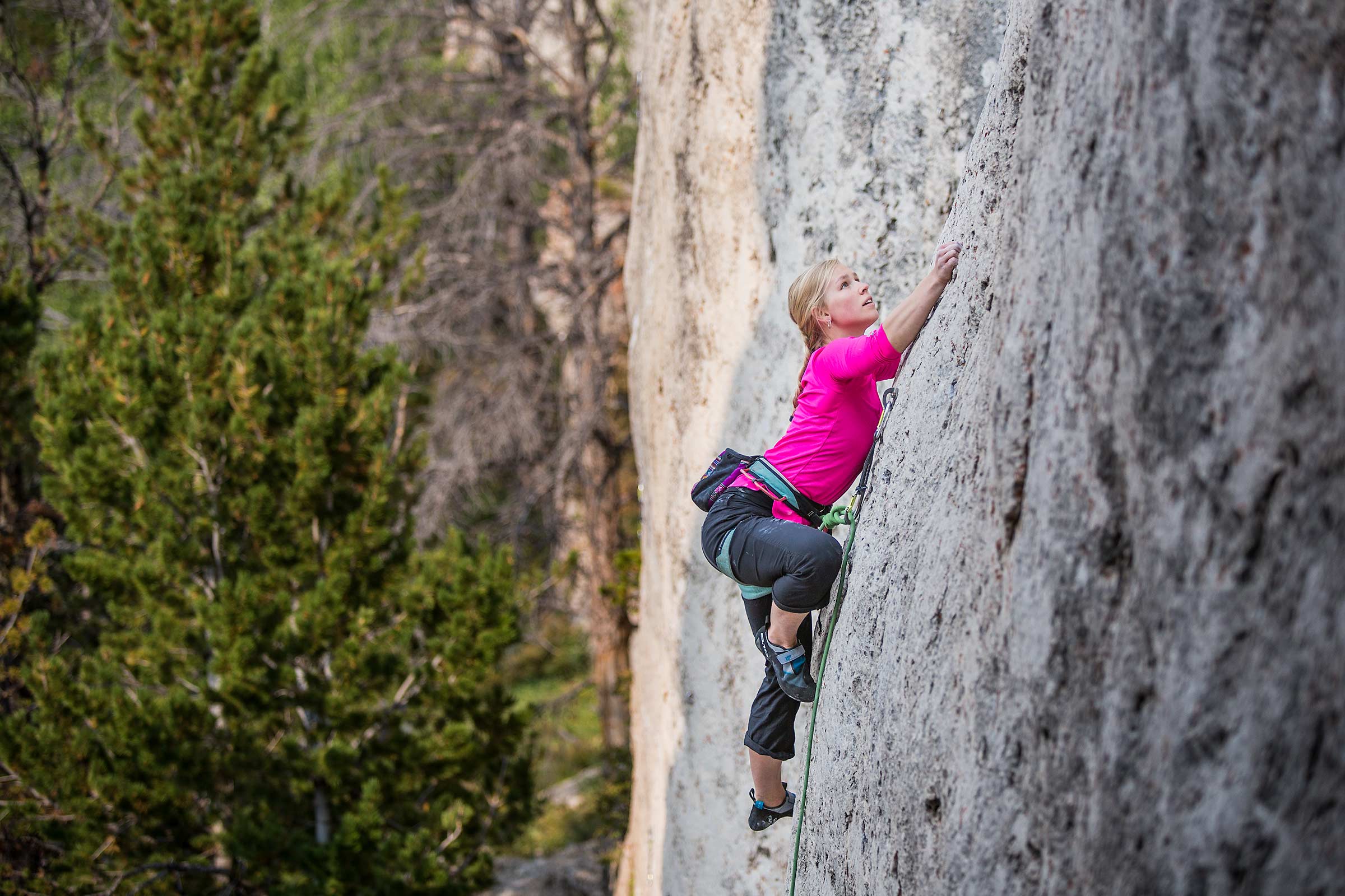 A young female college student rock climbing on a vertical white wall 