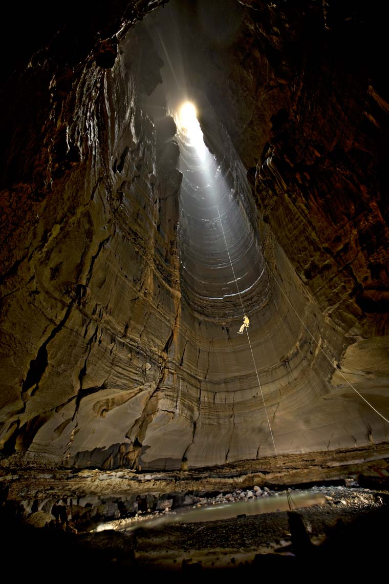 A shaft of light illuminating a caver rappeling into a giant cave chamber