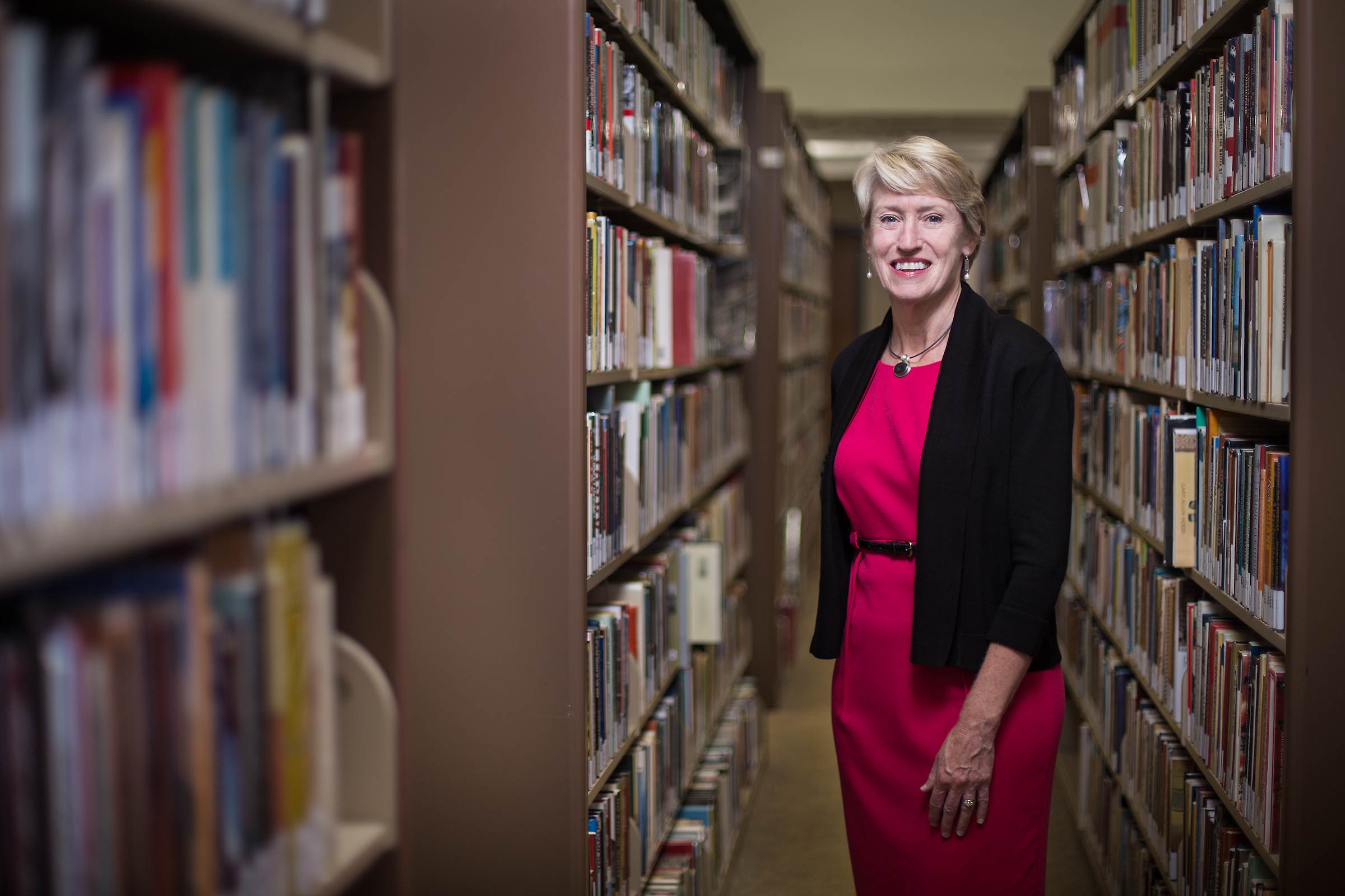 A female  president of a New England College posed on campus amid rows of books 