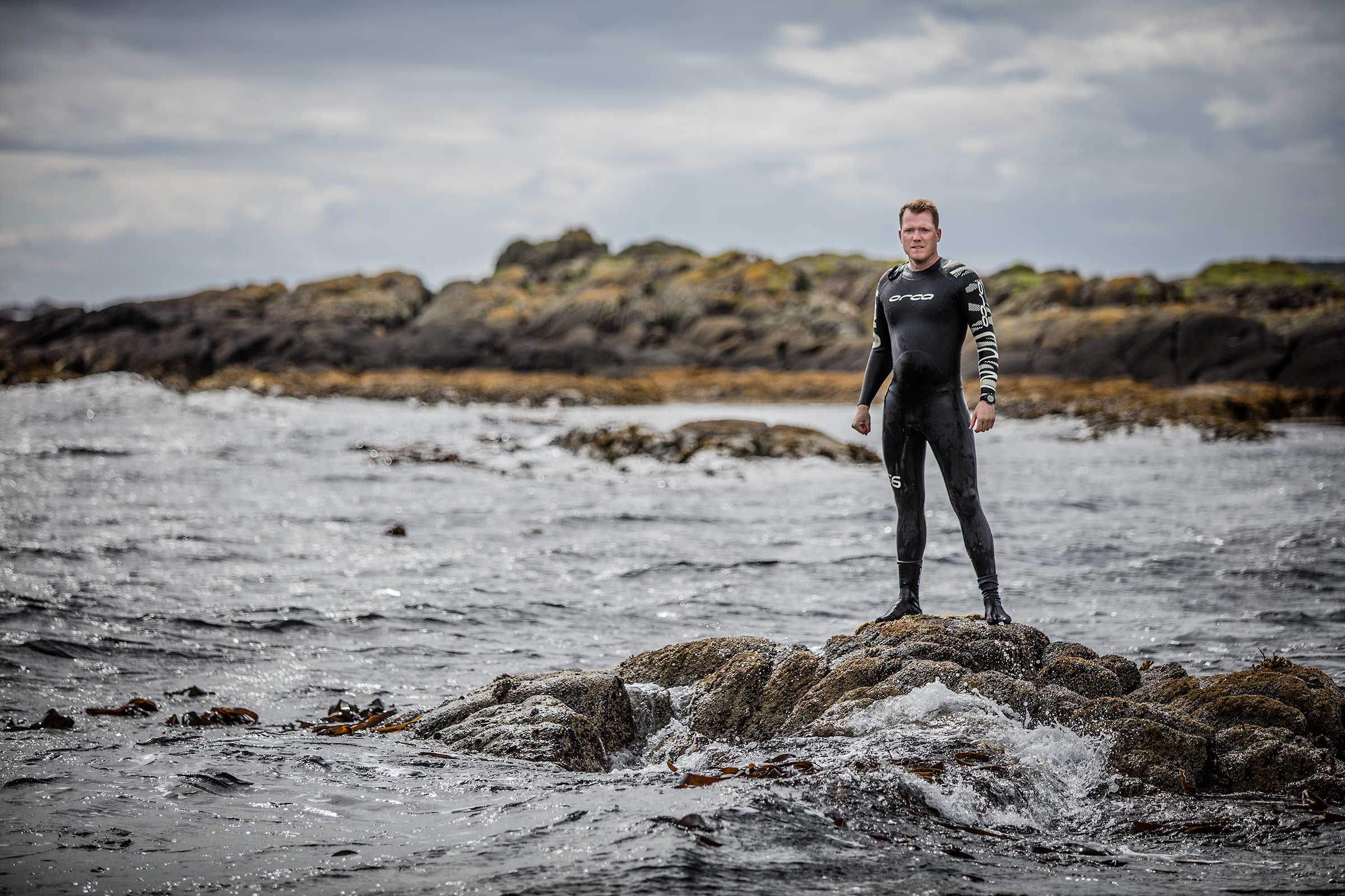 dramatic portrait of long distance open water swimmer on rocks among ocean waves