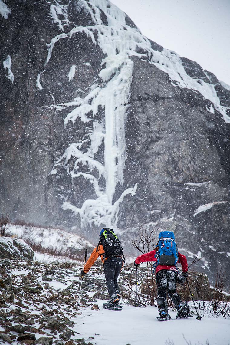 A pair of ice climbers ascends a steep hill with snowshoes during storm in Newfoundland