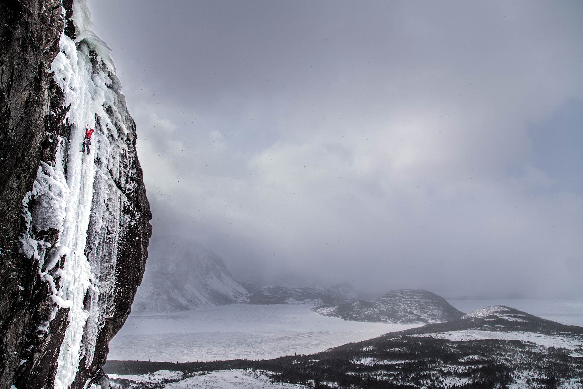 A dramatic panoramic landscape of an ice climber ascending a fjord in Newofoundland