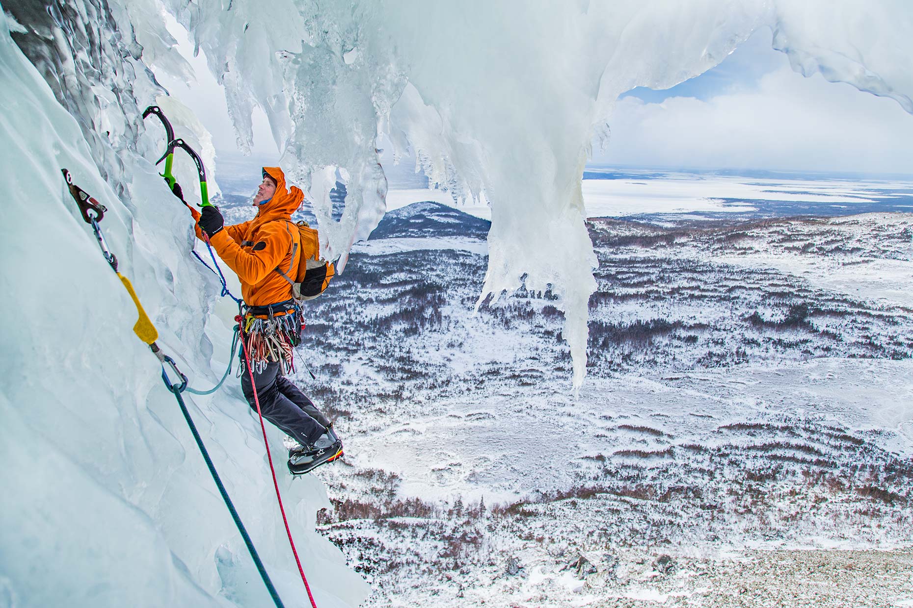 An ice climber navigates a bizarre windswept curtain of ice perched over a Newfoundland fjord