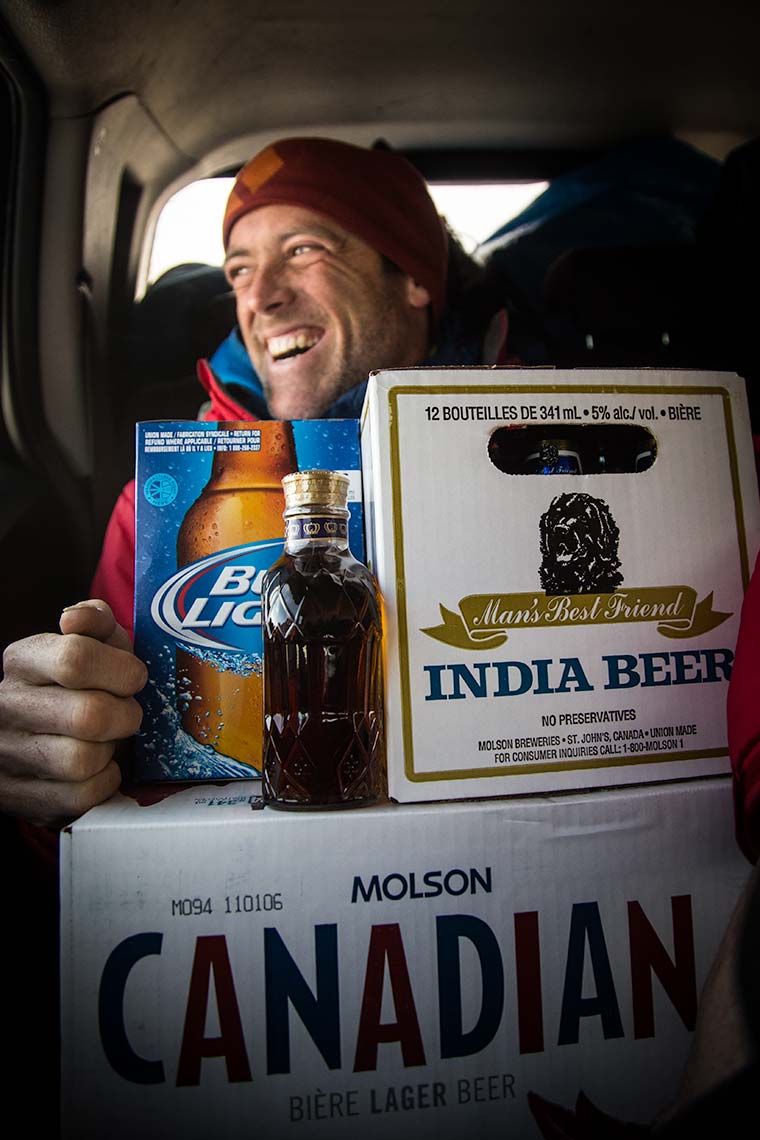 Closeup of an iceclimber laughing while packed into the car with a large pile of beer