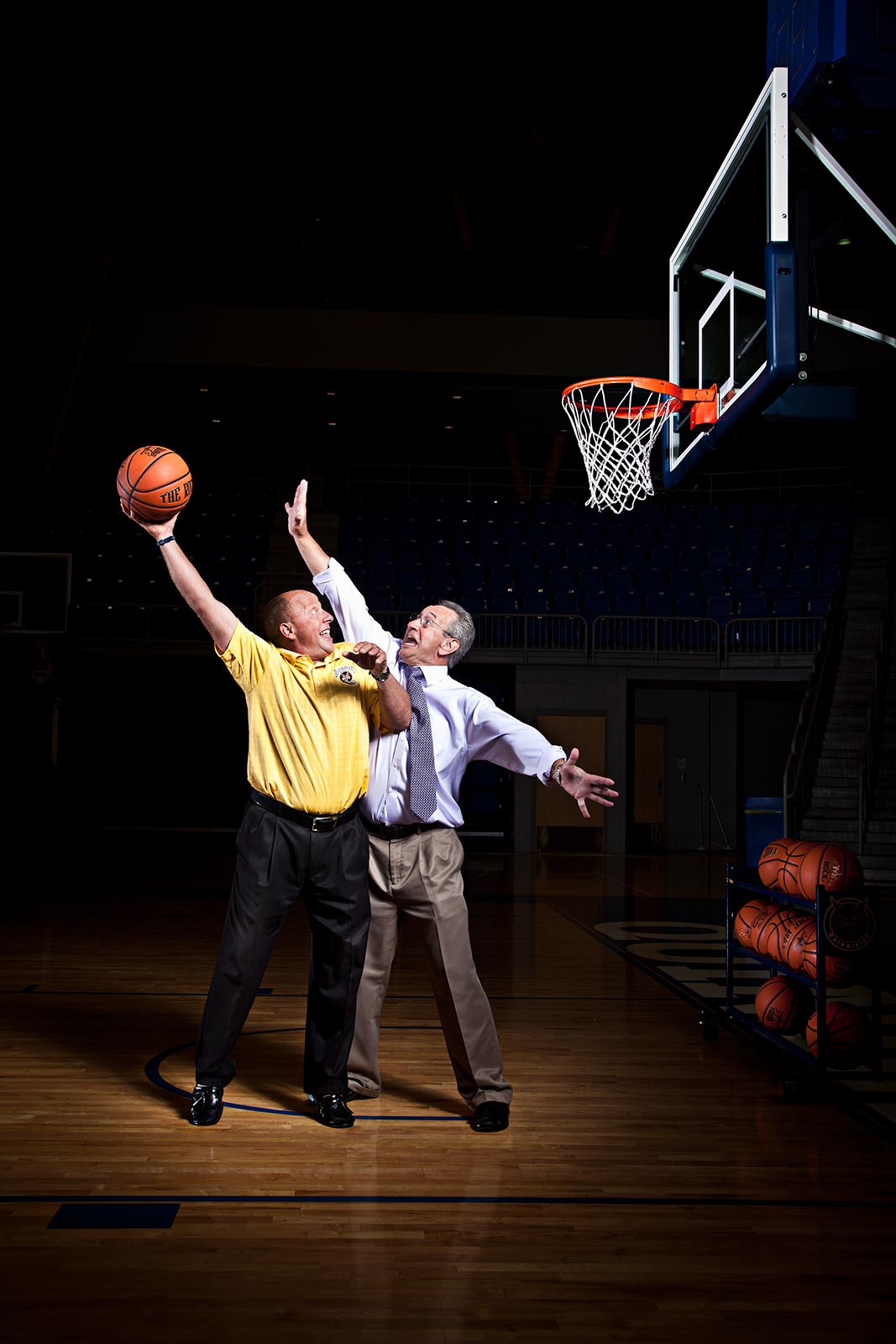 dramatic scene of two sports announcers playing basketball wearing suits in areana
