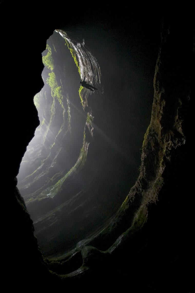 Dramatic view of an adventurer rappeling into a deep dark cave opeing