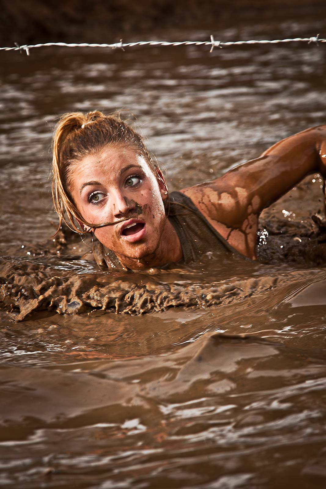 A fit athletic young woman swimming thru a mud obstacle as part of an adventure race in Connecticut