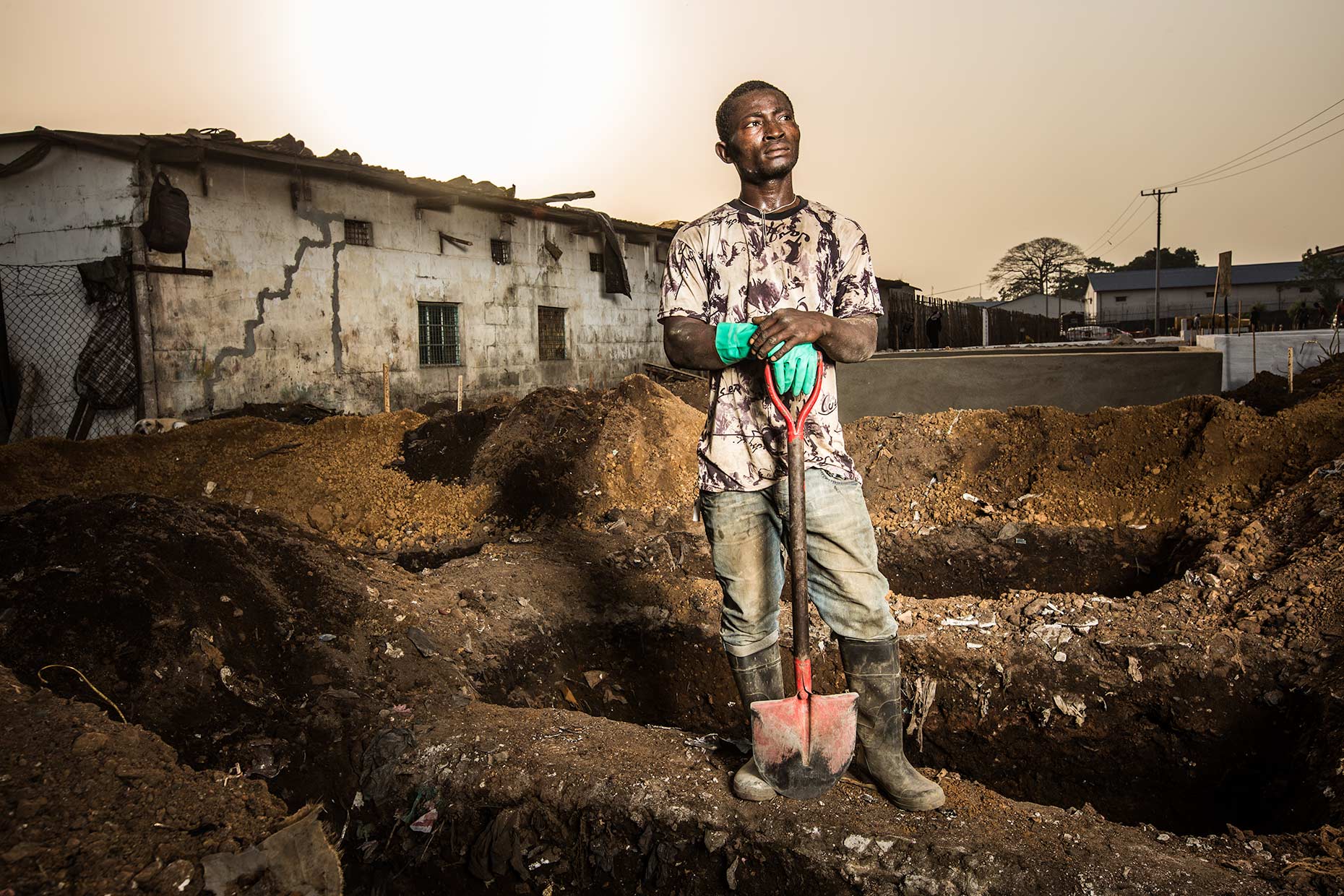 A worker stands next to a row of open graves awaiting Ebola Victims