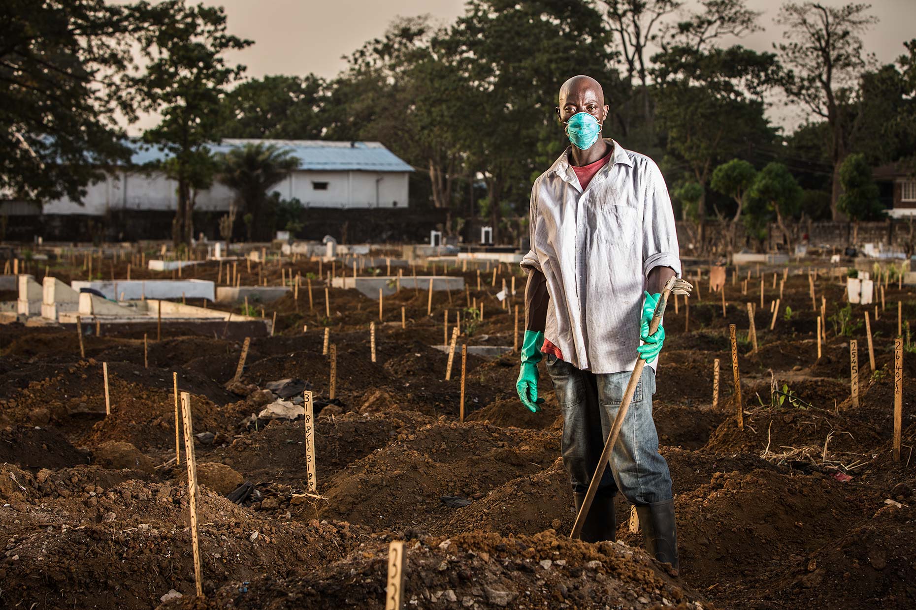 A worker wearing surgical mask and gloves while digging in a smokey Ebola graveyard