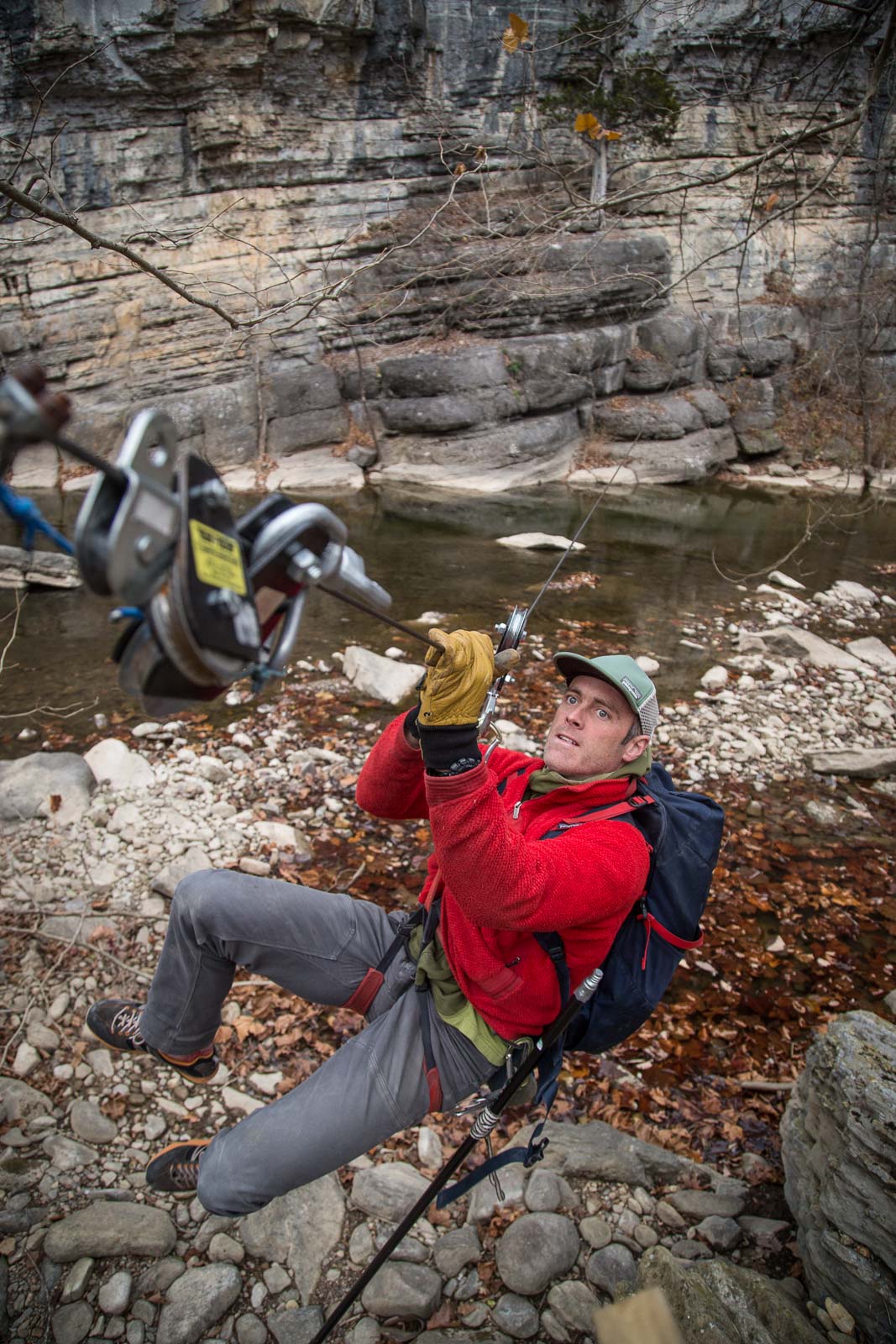 An adventure athlete pulls himself on a cable pulley above a swift river
