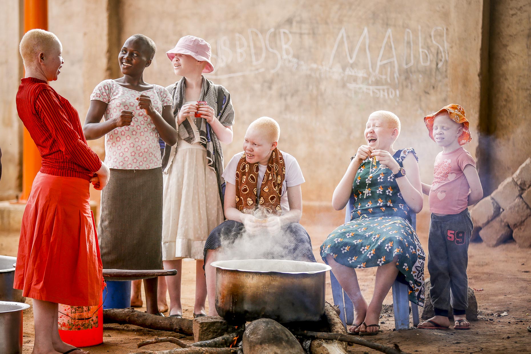A group of childern laughing together gathered around an outdoor kitchen in an orphanage in East Africa