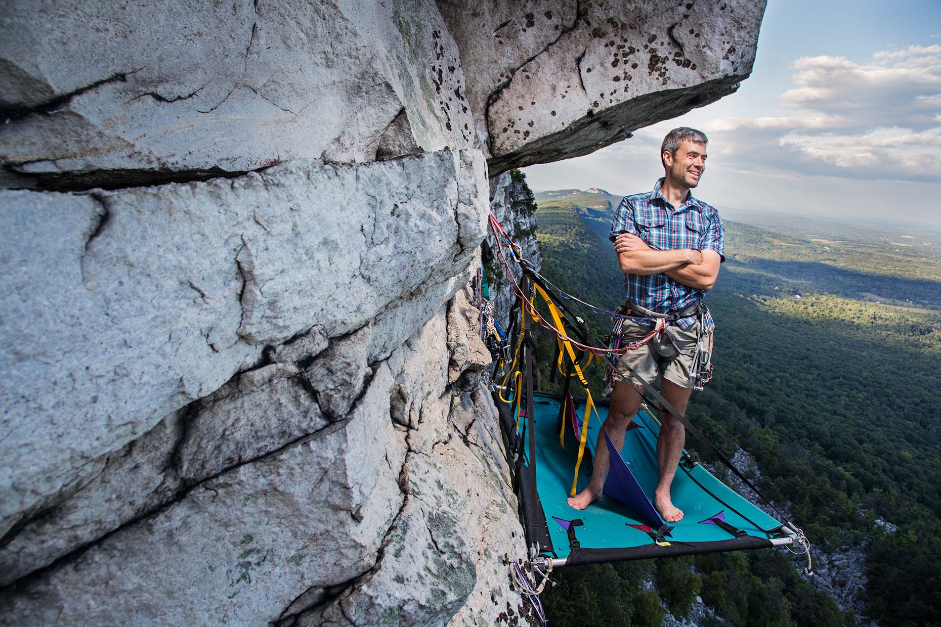 A confident portrait of a rock climber standing on a hanging ledge on a cliff in New york