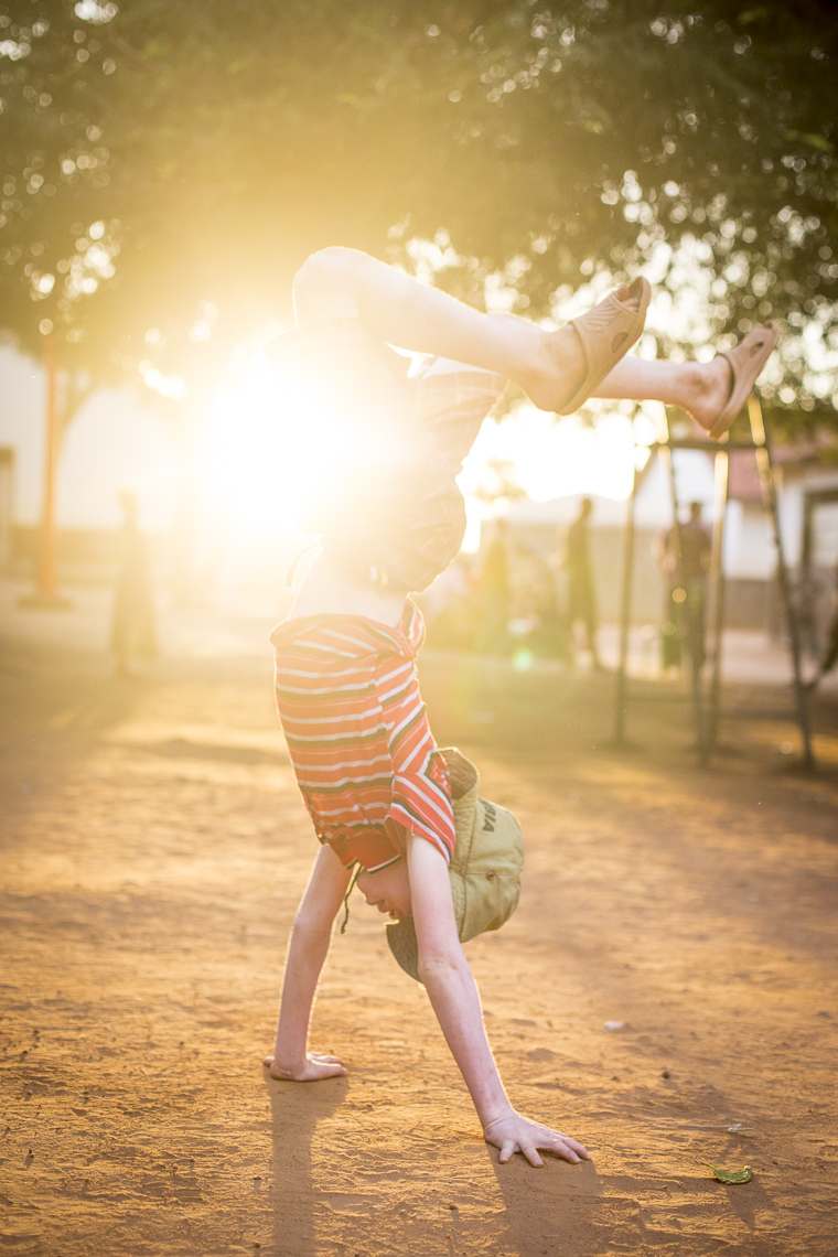 A young boy playful does a handstand in the setting sun in an East African school for Albino Children