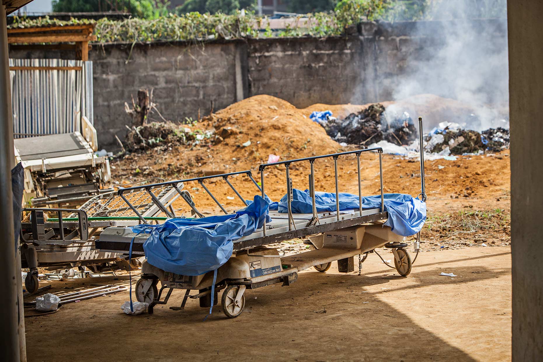 An empty gurney sits in front of a burning pile of medical waste at an Ebola hospital