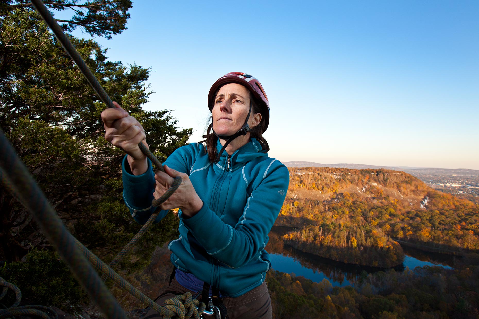 A middle aged woman pulls on a rope on top of a Connecticut cliff in winter