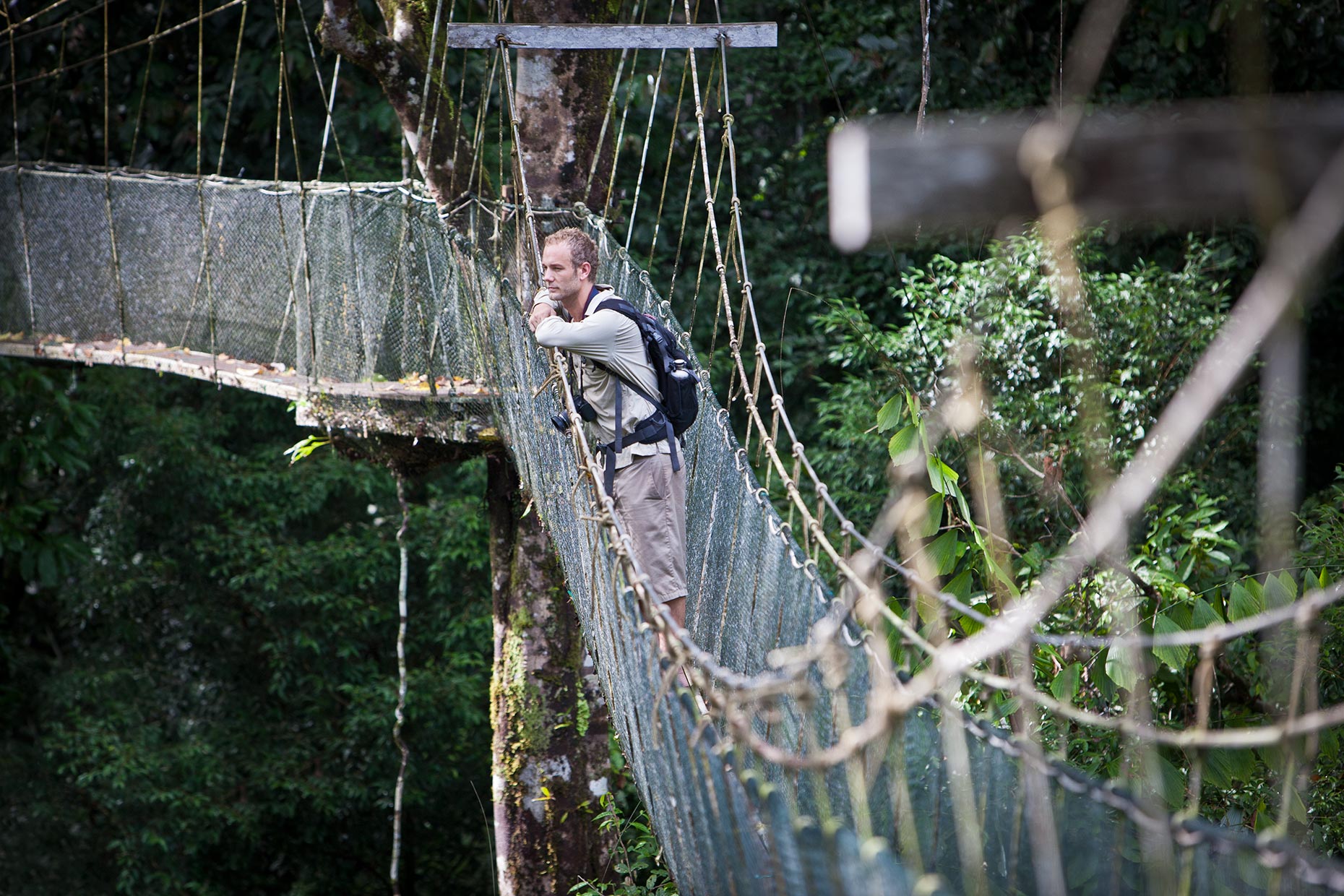 A young adventure tourist pauses on a swinign bridge to admire the view in Borneo