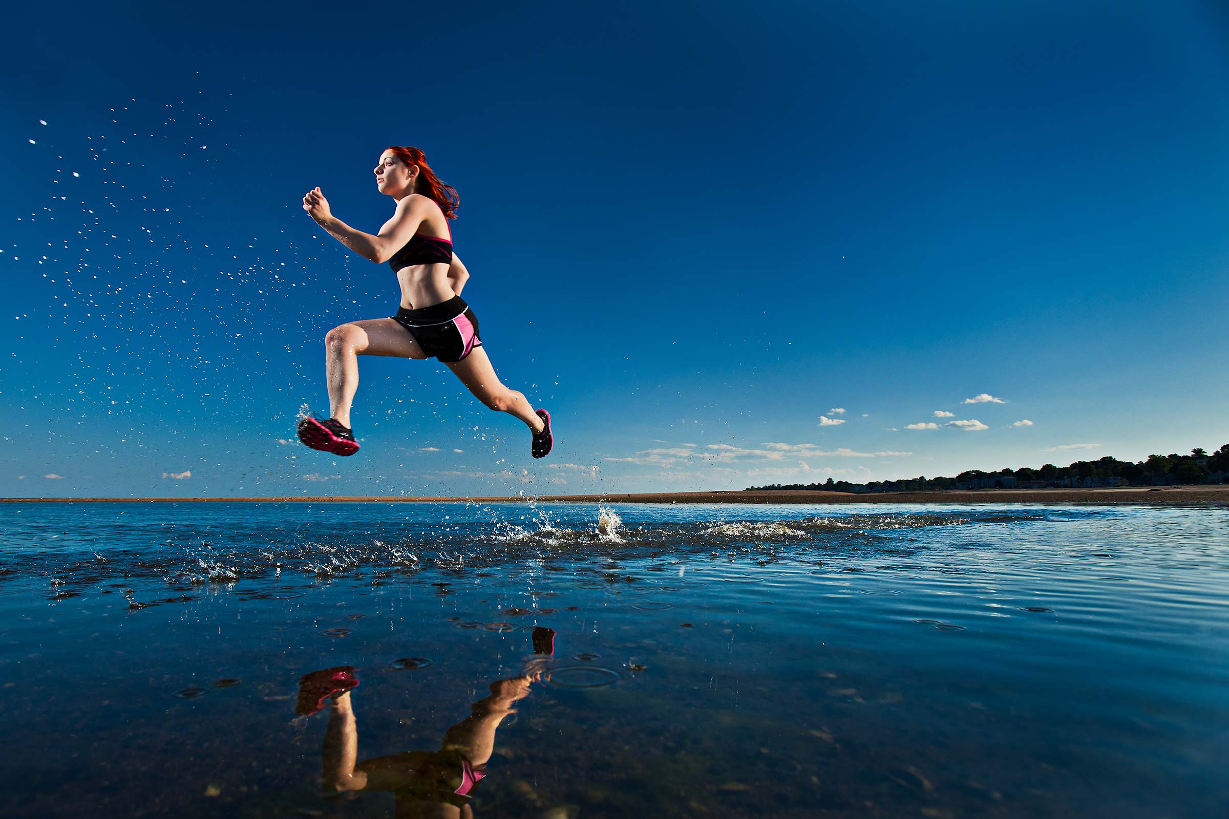a young female runner kicks up a spray of water while running on a Connecticut beach