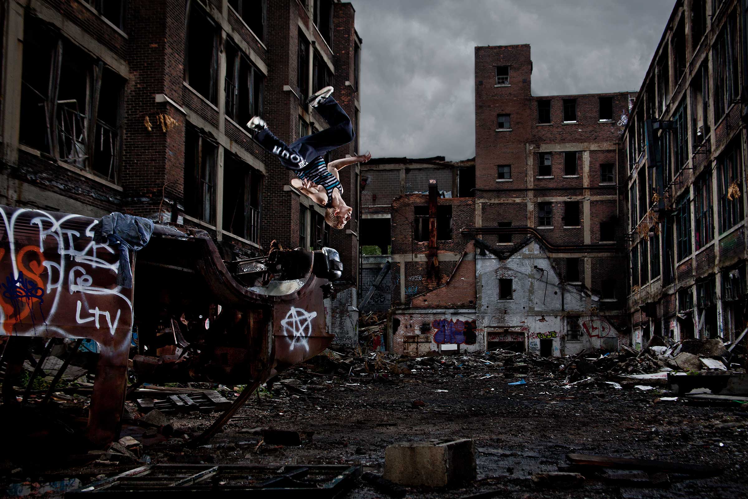 a young male parkour athelete does a flip off an abandoned car in an industrial location