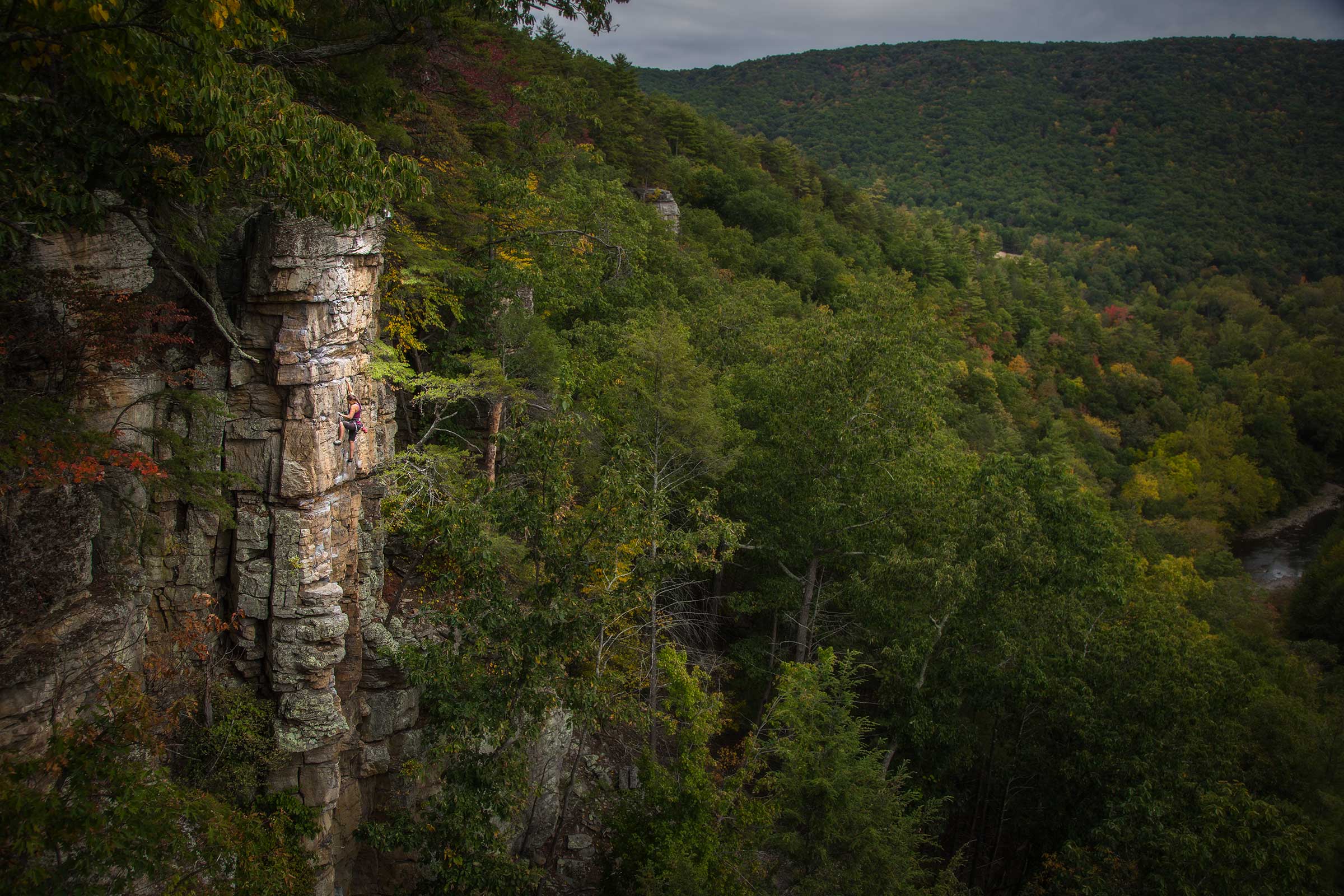 A panoramic view of a female rock climber with dramatic light in mountains in West Virgina