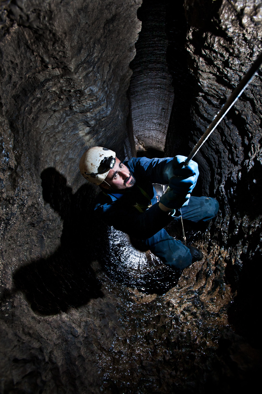 A overhead view of man ascending a rope out of a dark underground cave in New York 